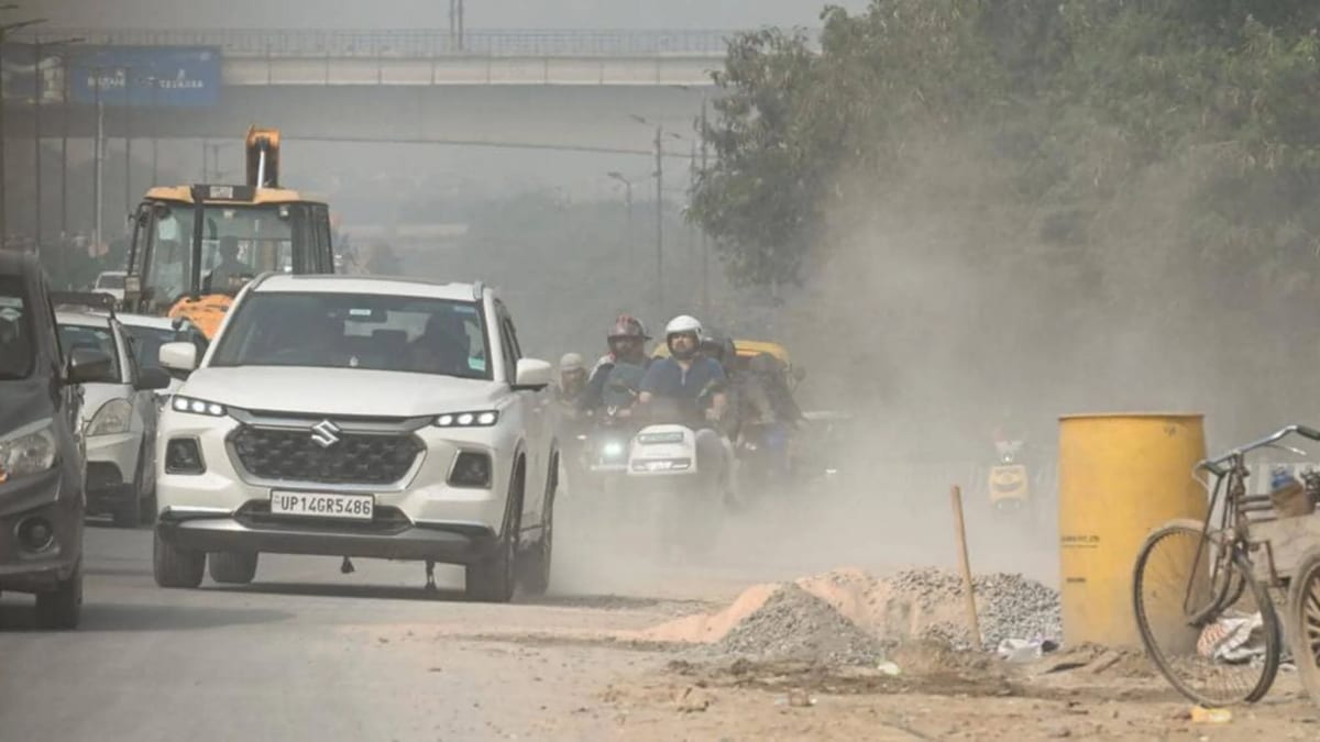 Vehicles pass through a dust-covered road amid construction-related air pollution in Delhi